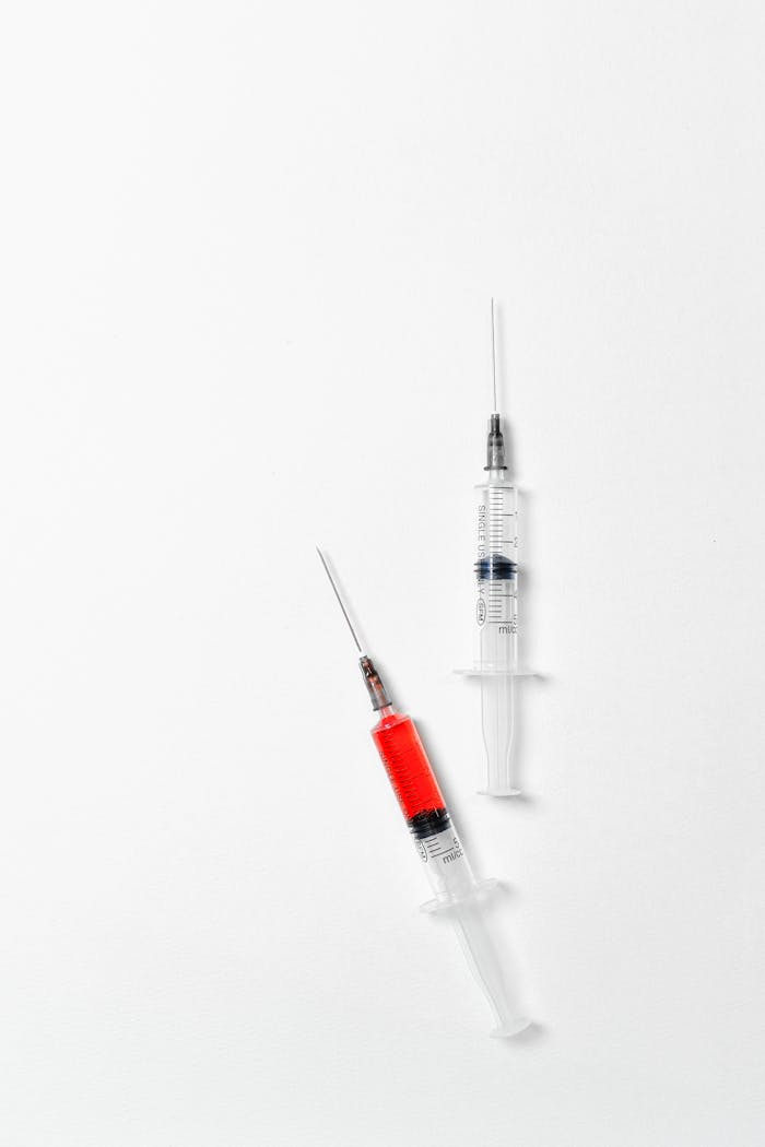 Close-up of syringes filled with red liquid on a white background, symbolizing medical treatment.